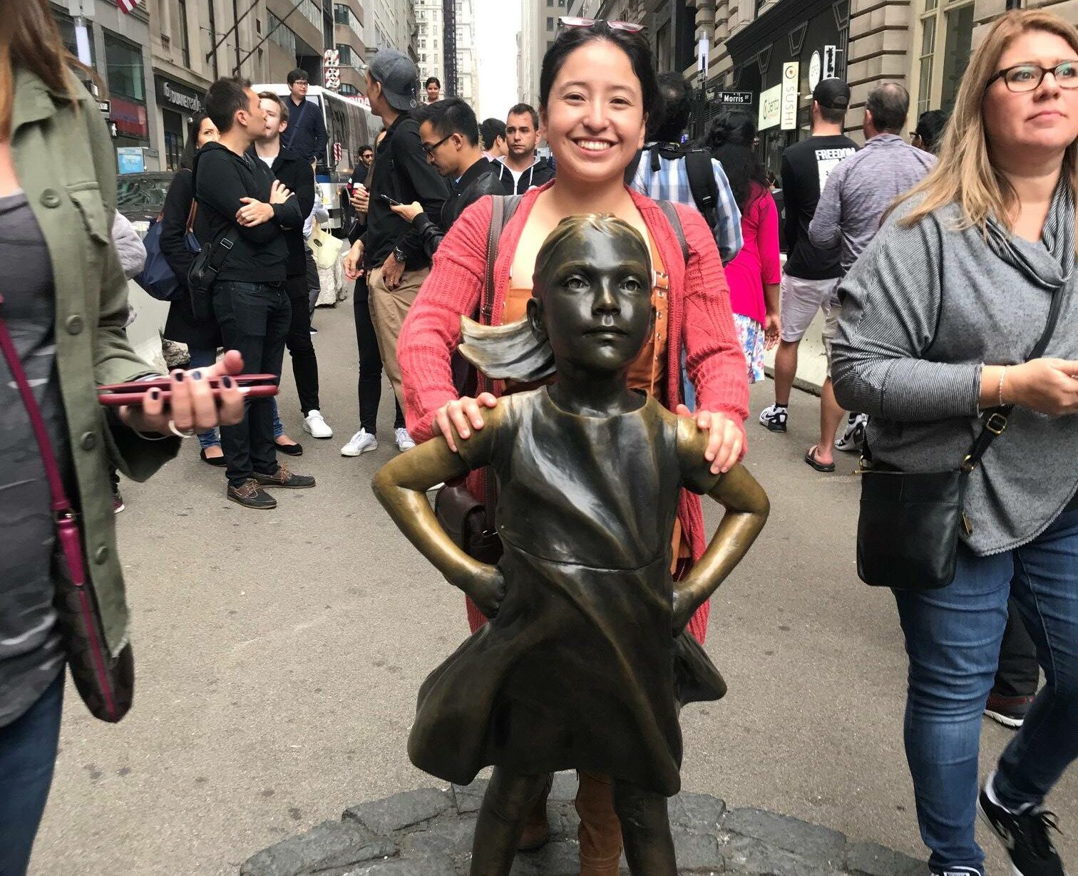 Photo of an international student standing behind New York's Fearless Girl Statue.